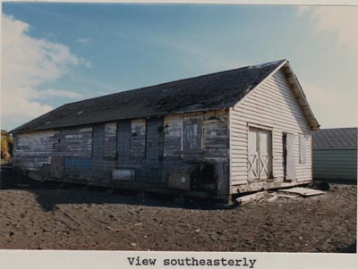 Photo of southeasterly view of the paint shop, a weathered white building.